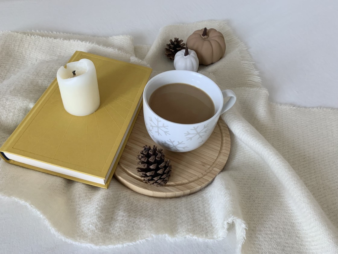 Cup of coffee on a book and white blanket and beside a fall scene